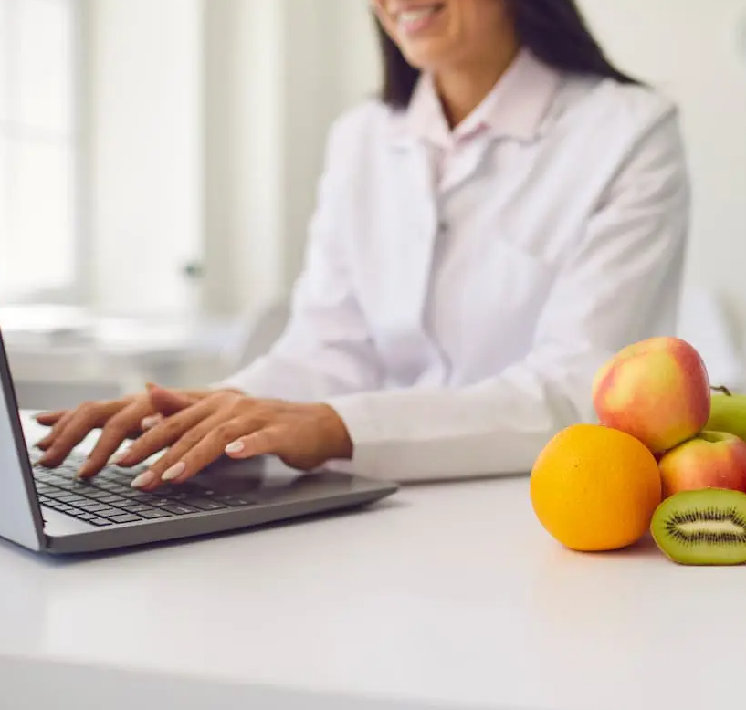 female typing on laptop next to oranges and kiwifruit